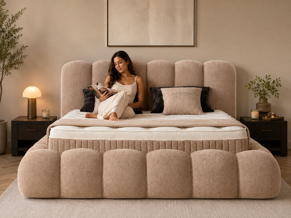 Vrouw leest op een bed met beige gestoffeerde rand, met kussens in haar rug